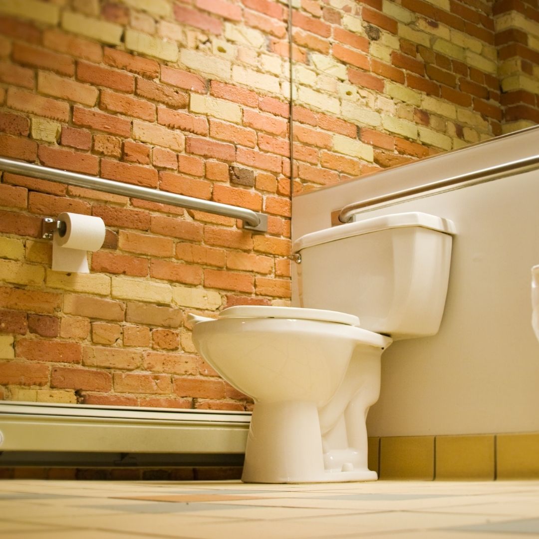 Toilet with mirror behind it and a brick wall next to it